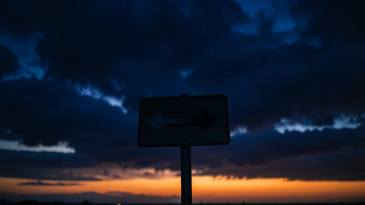 A single road sign pointing forward at dusk, navy sky with warm orange horizon